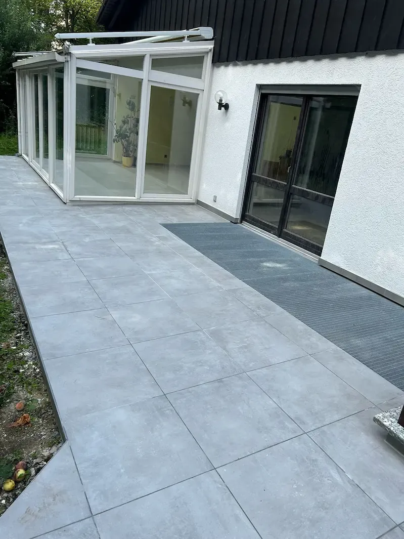 Terrasse mit großen grauen Fliesen vor einem Wintergarten